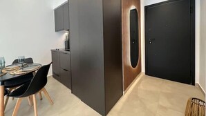 A modern kitchen with dark cabinetry, a dining table with chairs, and a black door. - BlueMotion - PortSuite (Piraeus)