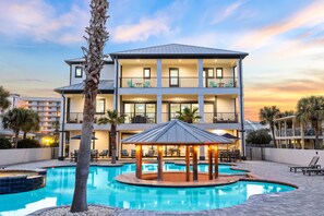 Un hotel de varios pisos con piscina, mobiliario exterior y un pabellón.