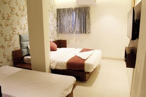 Une chambre d’hôtel avec deux lits, une tête de lit en bois, un téléviseur fixé au mur et une fenêtre avec des rideaux.