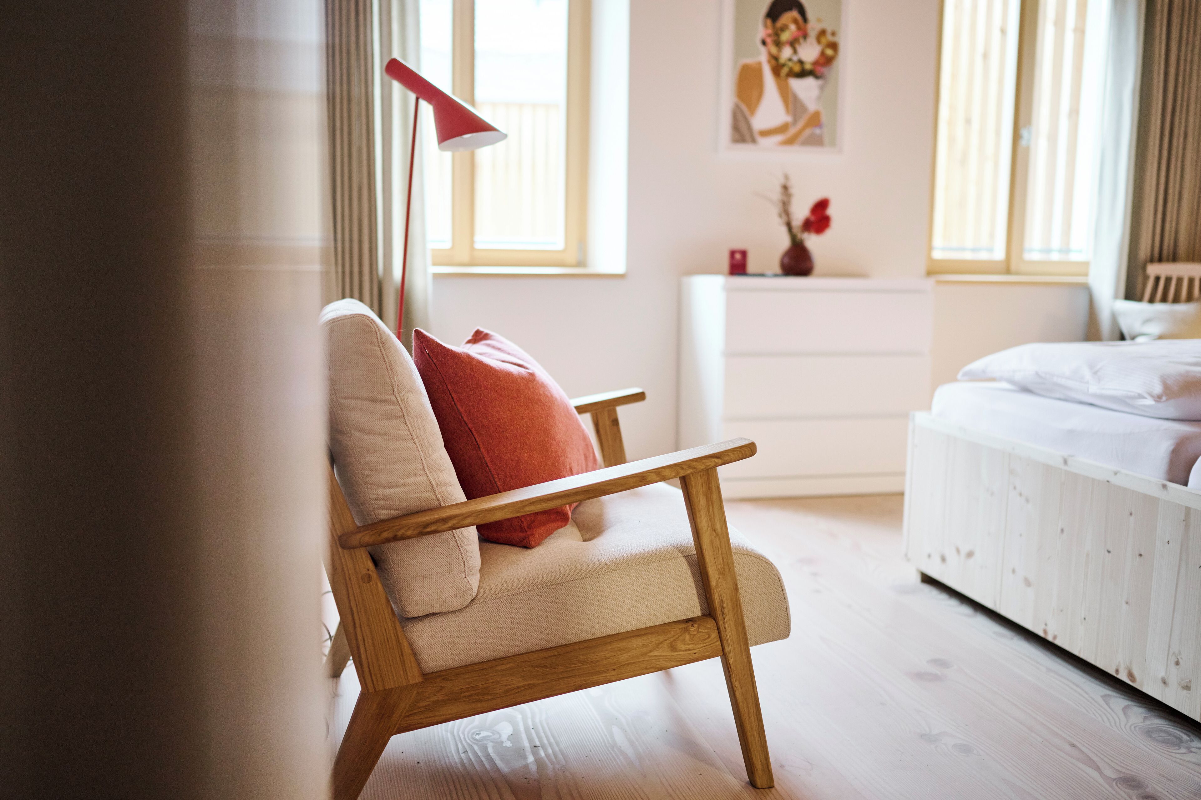 A bedroom with a wooden chair, a bed, a nightstand, and a red floor lamp.