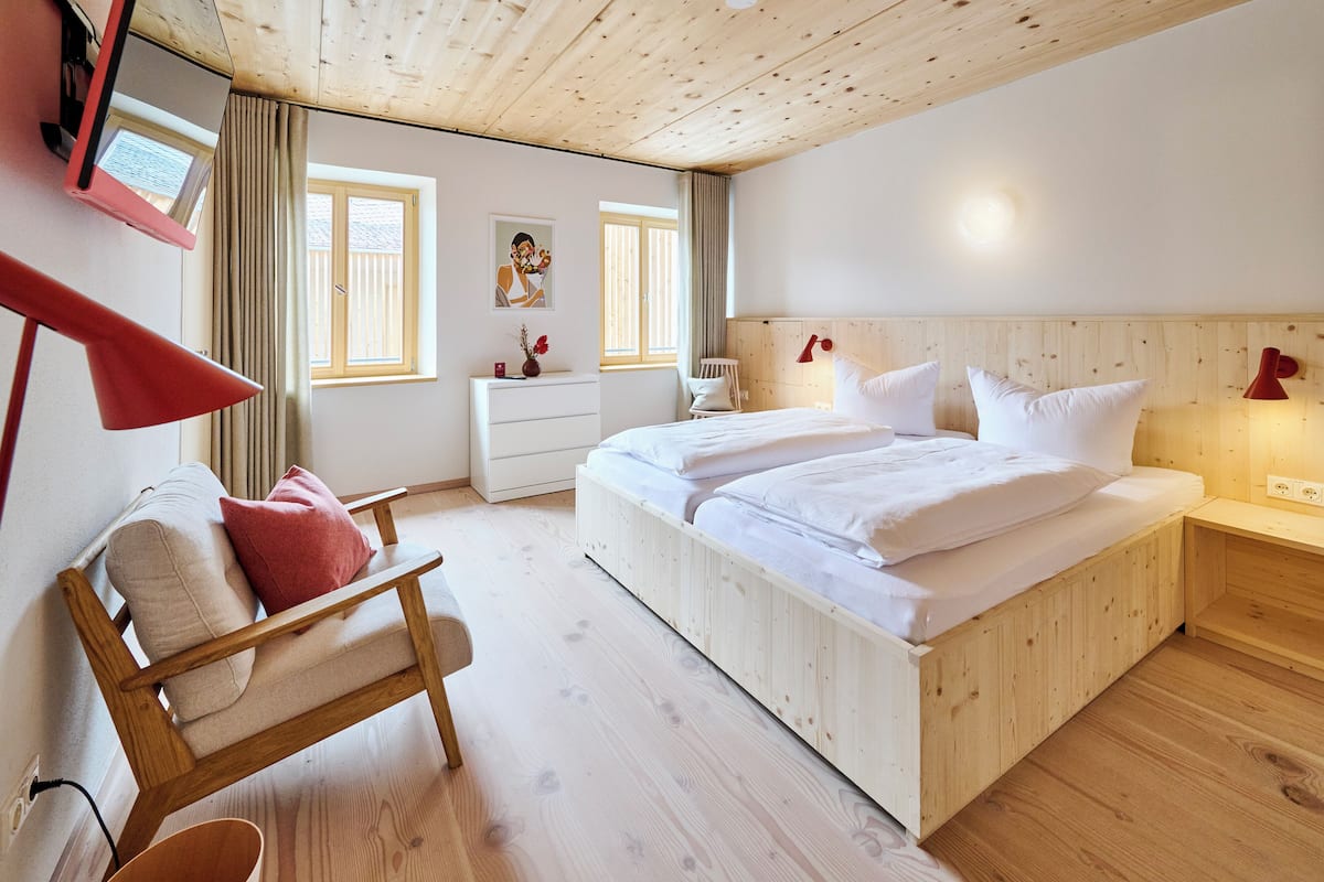A wooden-paneled bedroom with a bed, bedside tables, a chair, and a desk.