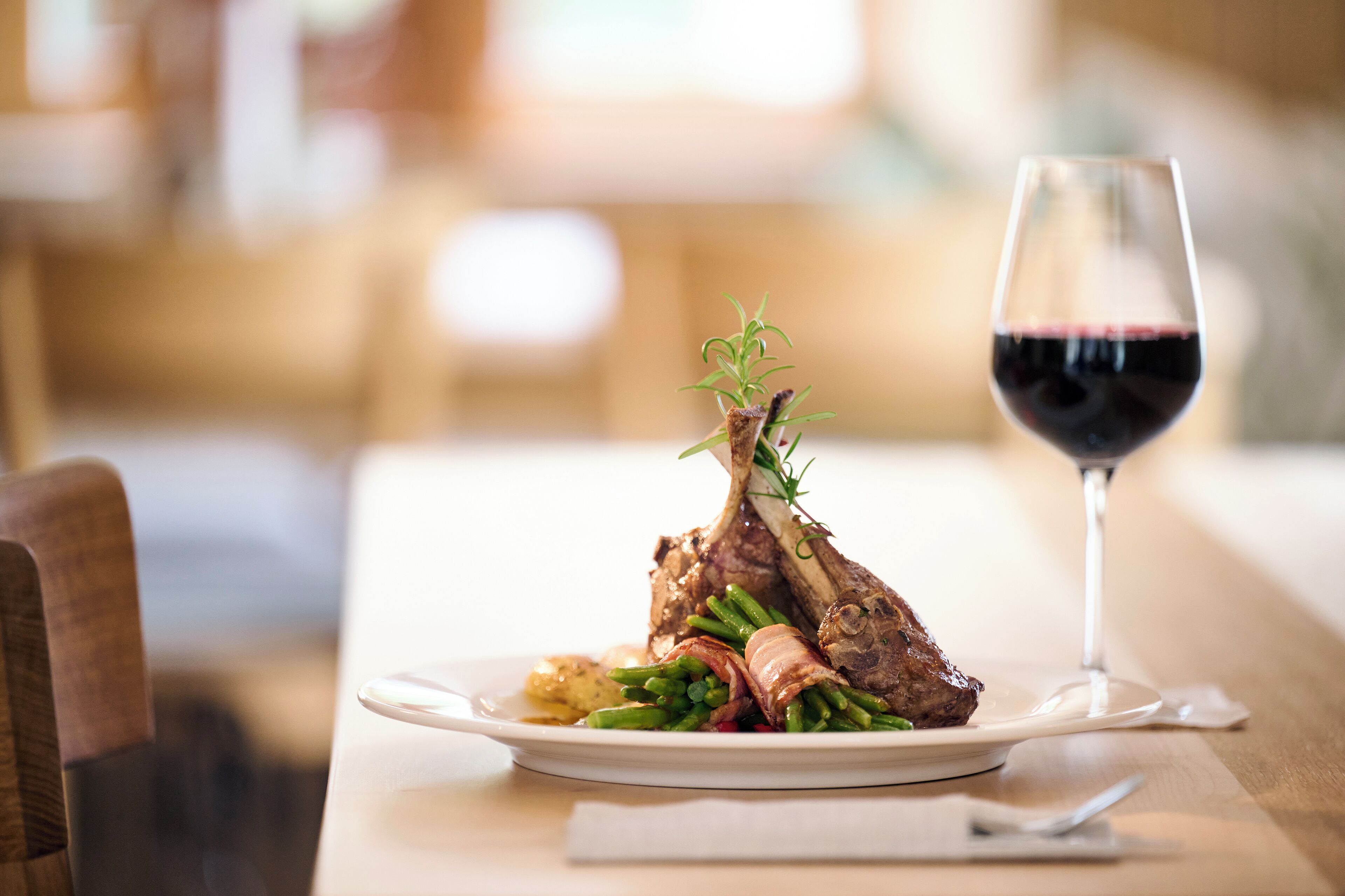 Un plato con un jarrete de cordero, judías verdes y patatas, acompañado de una copa de vino tinto.