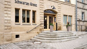 Un edificio con el nombre 'Schwarzes Kreuz' en la fachada, que presenta una escalinata de piedra que lleva a la entrada y dos macetas con plantas en los escalones.