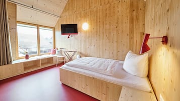 Una habitación tipo cabaña de madera con cama, televisor montado en la pared y ventana con vista al exterior.