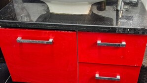 A bathroom with a white sink, black countertop, and red cabinets.