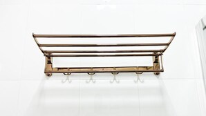 A metallic towel rack with four hooks on a white tiled floor.