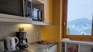 A compact kitchen with a microwave, coffee maker, and sink. A window offers a view of mountains. - Cozy apartment near slopes, valley view (La Plagne Montchavin Les Coches)