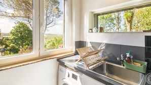 A kitchen with a washing machine, a sink, and a window with a view of trees and a building.