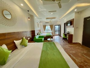A hotel room with a large bed, green and white bedding, a green sofa, a small round table, a TV, and a ceiling fan. - Wanna Stay Rishikesh (Rishikesh)