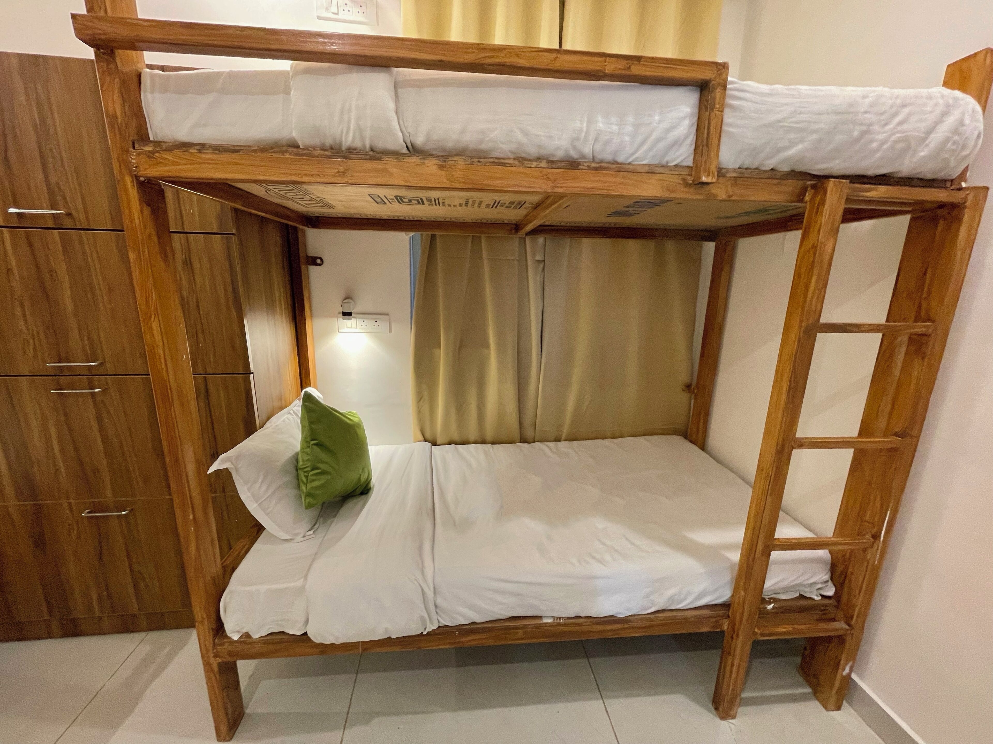 A bunk bed with a ladder, a wooden wardrobe, and a curtain.