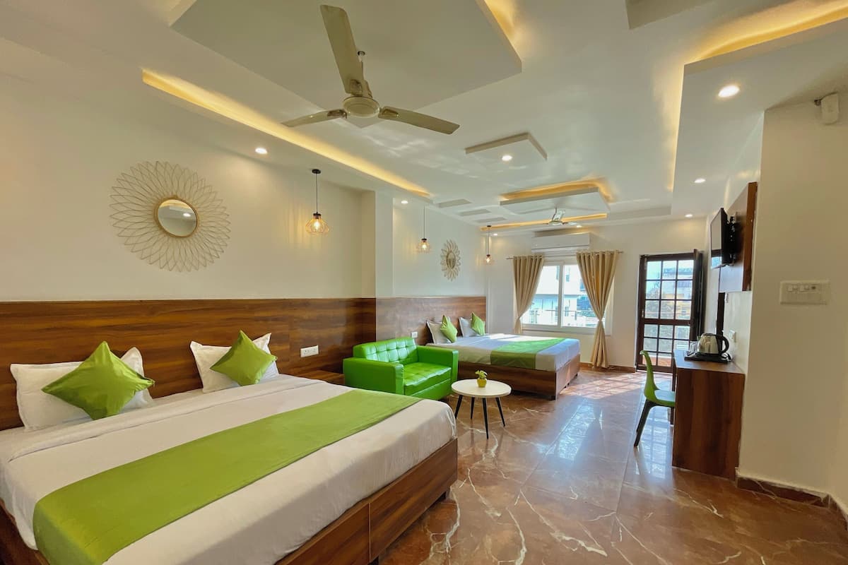 A hotel room with two beds, a green sofa, a small table, and a TV.