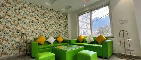 A modern living room with a green sofa set, a coffee table, and a patterned wallpaper.
