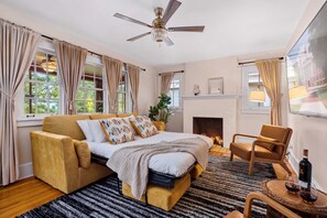 Um quarto com cama, sofá, poltrona, lareira e ventilador de teto.