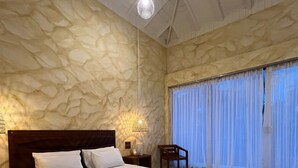 A spacious bedroom with a large bed, a stone-patterned wall, a chandelier, and a view through sheer curtains. - Triton Dondra (Dondra)