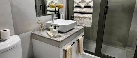 Ein modernes Badezimmer mit Waschbecken, Spiegel, Toilette und einer Duschkabine aus Glas.