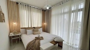 Un dormitorio moderno con una cama grande, mesitas de noche, un banco y cortinas de gasa.