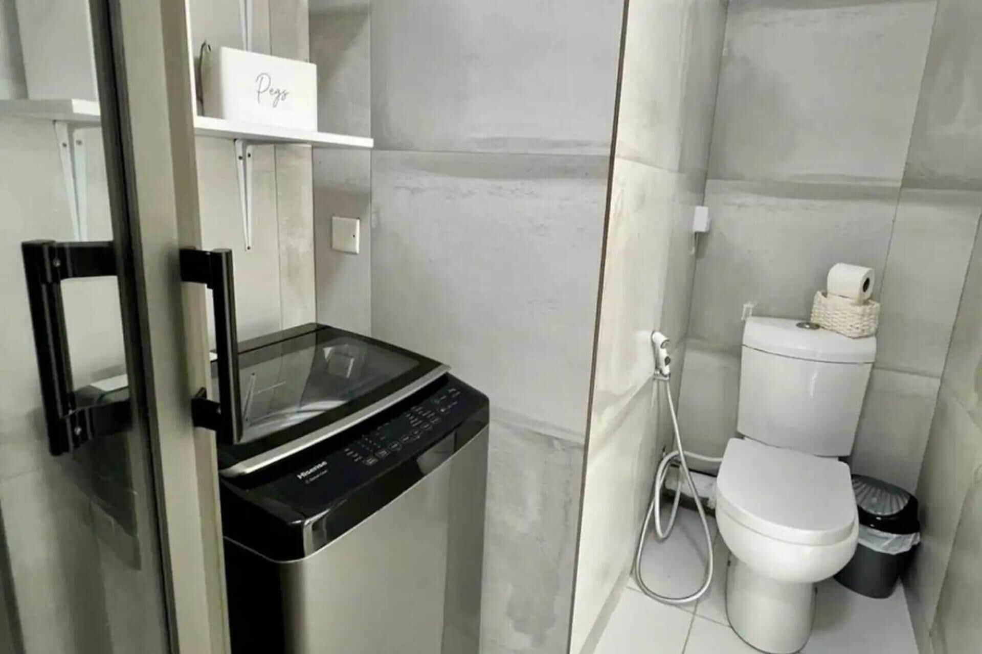 A compact bathroom with a glass shower enclosure, a toilet, and a compact washing machine.