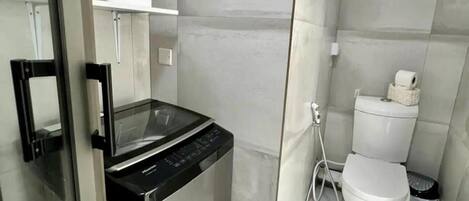 A compact bathroom with a glass shower enclosure, a toilet, and a compact washing machine.