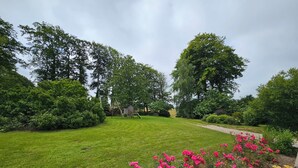 A well-maintained garden with a grassy lawn, a wooden play structure, and a variety of flowering plants.