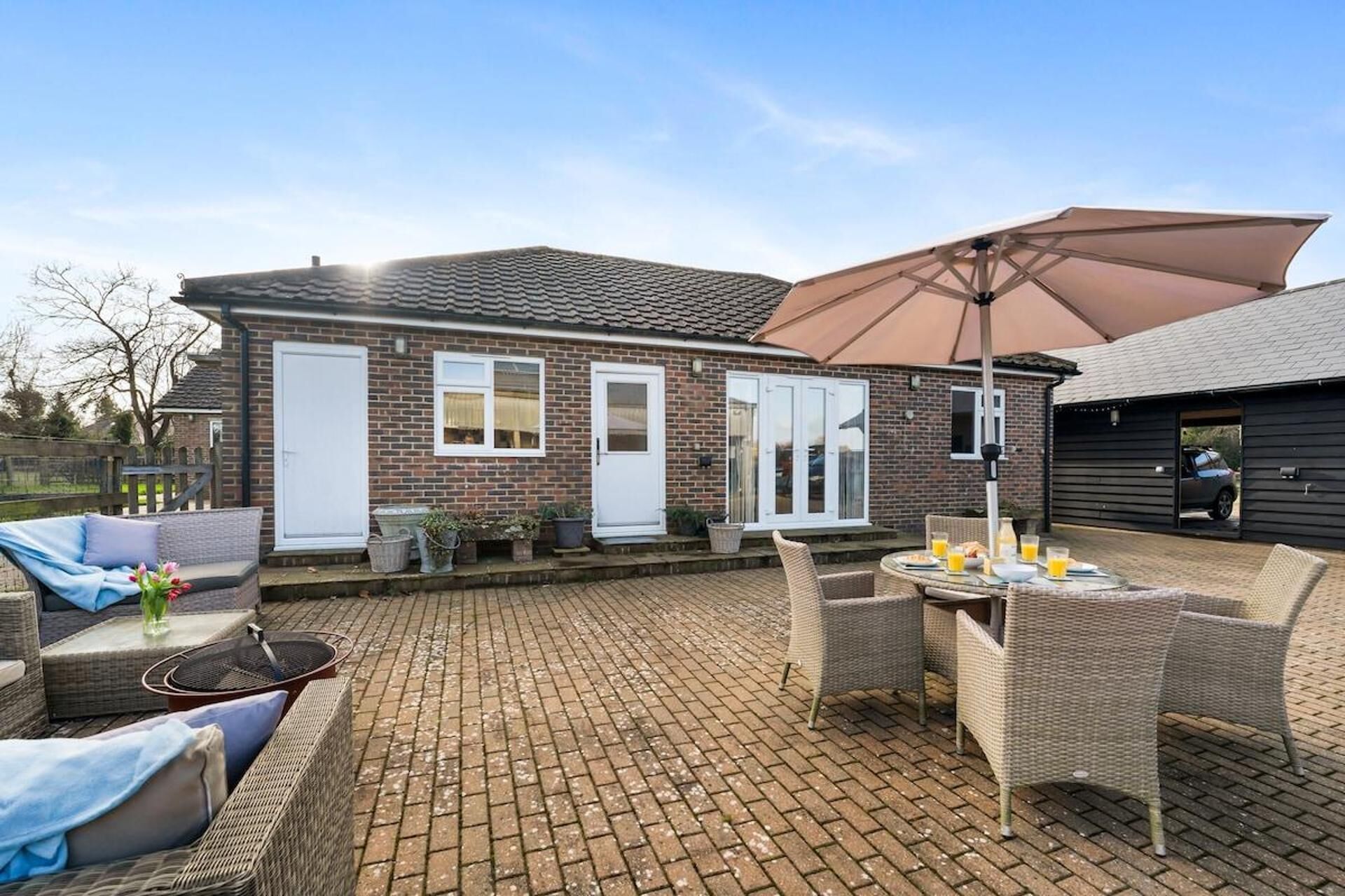 Un espace patio aménagé avec des meubles en osier, une table où sont disposées des boissons et un grand parasol.