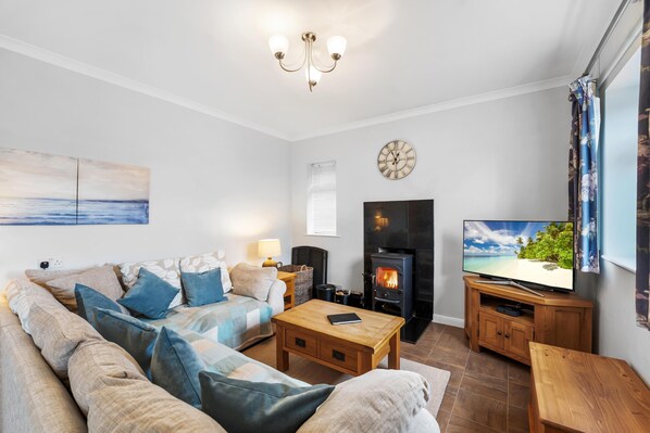 A living room with a sofa, coffee table, TV, fireplace, and artwork on the wall. - Chickens, Local Pubs and Country Walks! (Canterbury)
