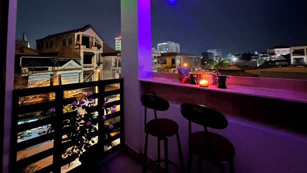 A balcony with a view of a cityscape at night, featuring a railing, a table with candles, and two bar stools. - Canary Homestay (Hue)