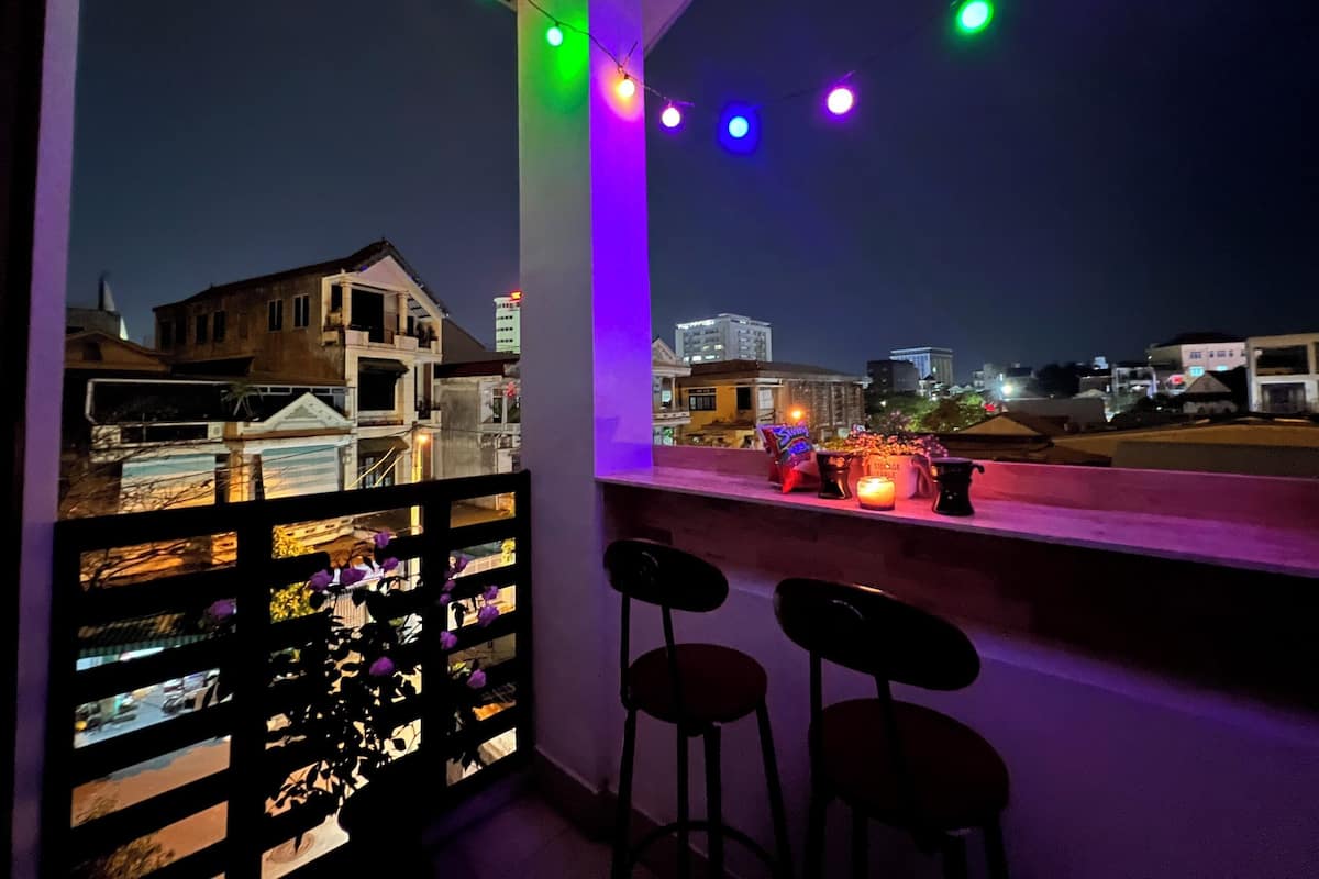 Ein Balkon mit Blick auf eine beleuchtete Stadtlandschaft, mit Geländer, Tisch und Kerzen sowie zwei Barhocker.