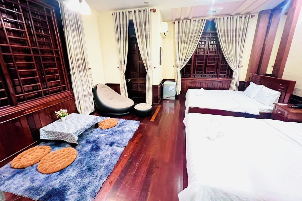 Ein Hotelzimmer mit zwei Betten, einem Massagesessel, einem kleinen Tisch mit Pflanze und einem blauen Teppich mit kreisförmigen Mustern.