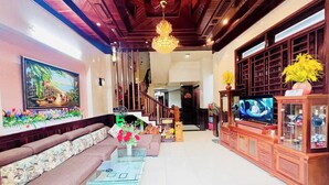 A spacious living room with a wooden ceiling, a large sofa, a glass coffee table, a television, and a decorative plant. - Canary Homestay (Hue)