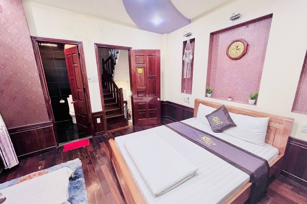 Quarto de hotel com uma cama grande, um guarda-roupa de madeira, uma secretária pequena e um banheiro com vaso sanitário e pia.