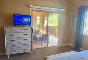 A room with a sliding glass door leading to a balcony, a wooden dresser, and a television displaying weather information. - First Floor..Mountain Views..Next to WestWorld (Scottsdale)