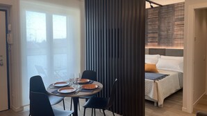 Moderni hotellihuone, jossa on ruokailutila. Tilaan kuuluu pyöreä ruokapöytä, johon on katettu neljälle, tummat tuolit ja väliseinä.