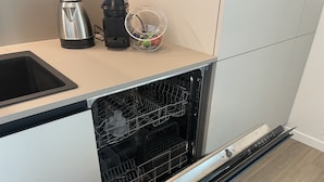 Moderni keittiö, jossa on astianpesukone, vedenkeitin ja lasinen säilytysastia työtasolla.