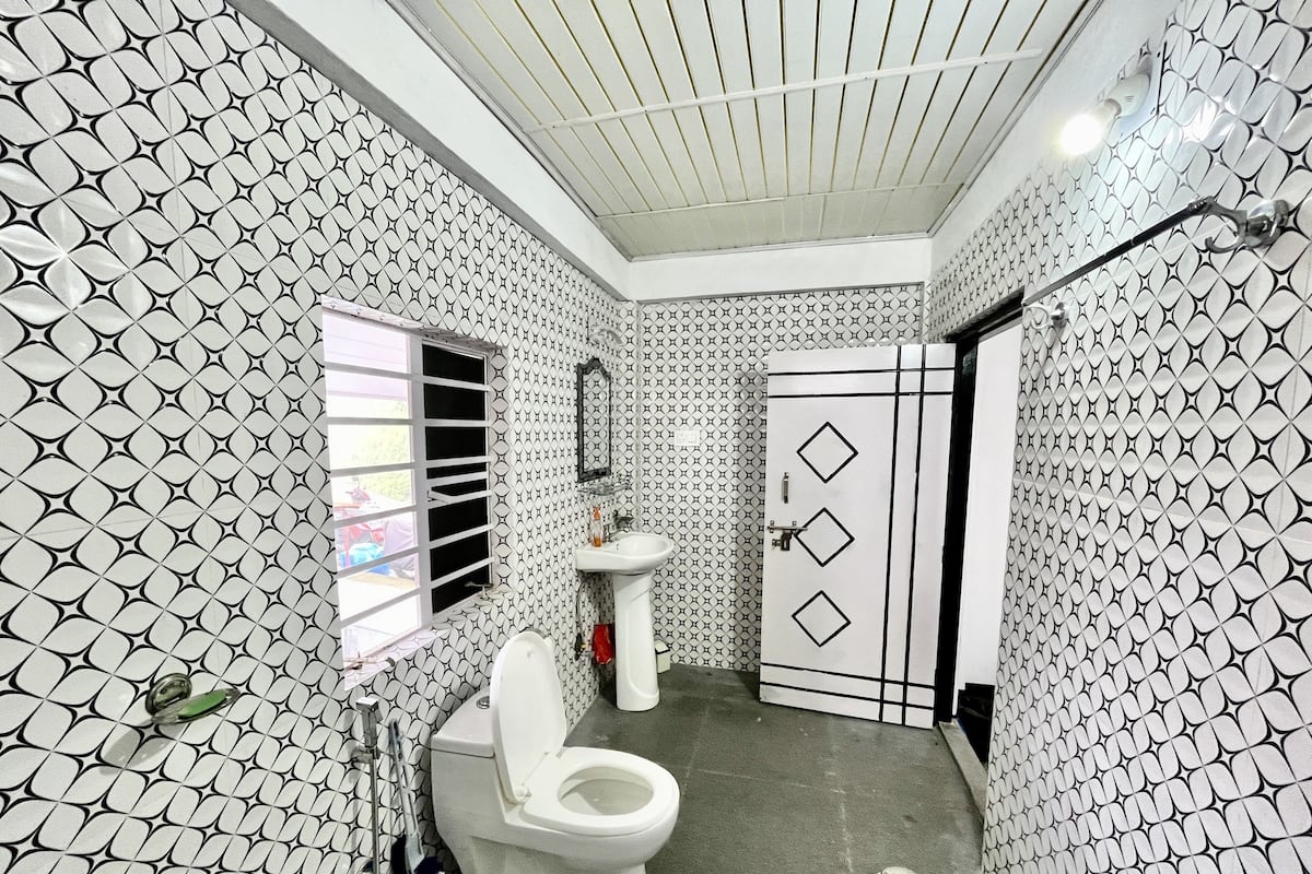 Un baño con pared estampada, inodoro, lavabo y puerta con abertura en forma de diamante.