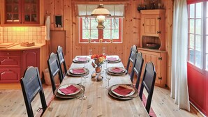 A wooden dining table set for six with red napkins, surrounded by black chairs. A window with a view of greenery is above the table, and a wooden cabinet is to the right. - Beautiful home in Rjukan with sauna (Rjukan)