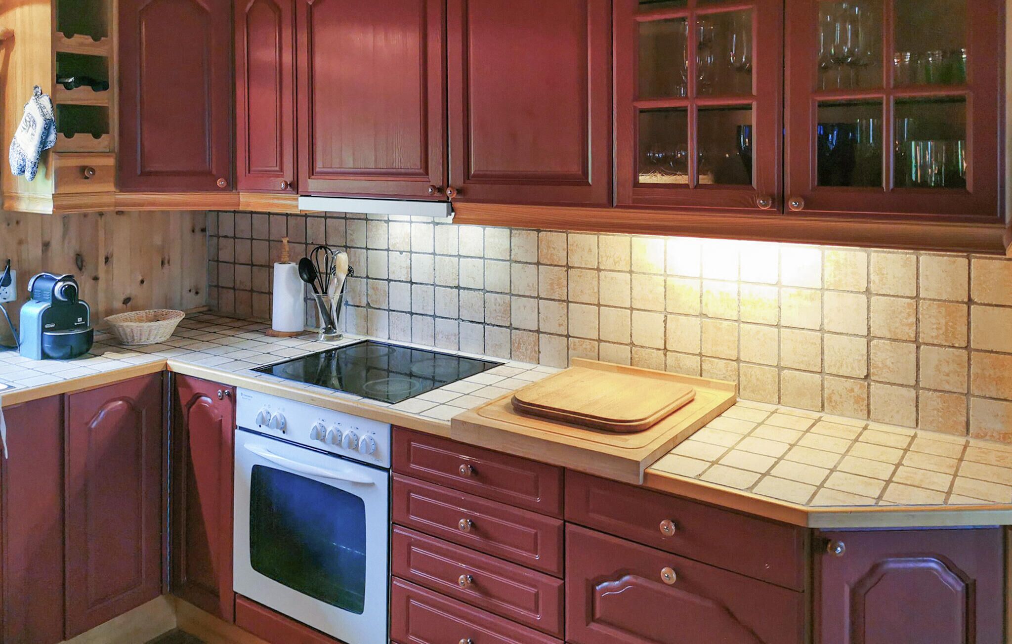 A kitchen with red cabinets, a stove, an oven, a sink, and a tiled backsplash.
