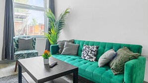 A living room with a green sofa, a coffee table, a potted plant, and a chair. - 3br-sleeps8-parking-wifi-closestation (Corby)