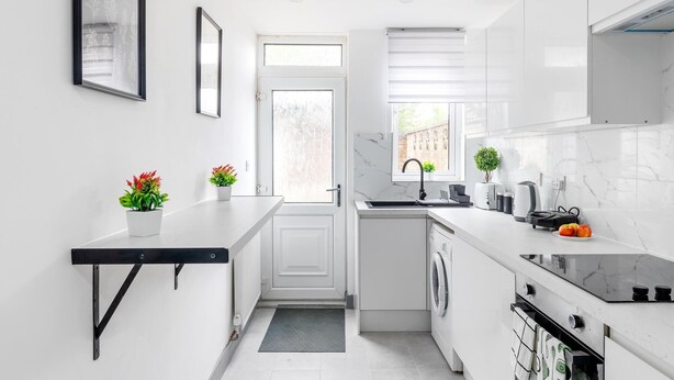A modern kitchen with white cabinetry, a built-in oven, a sink, and a window with blinds. - 3br-sleeps8-parking-wifi-closestation (Corby)