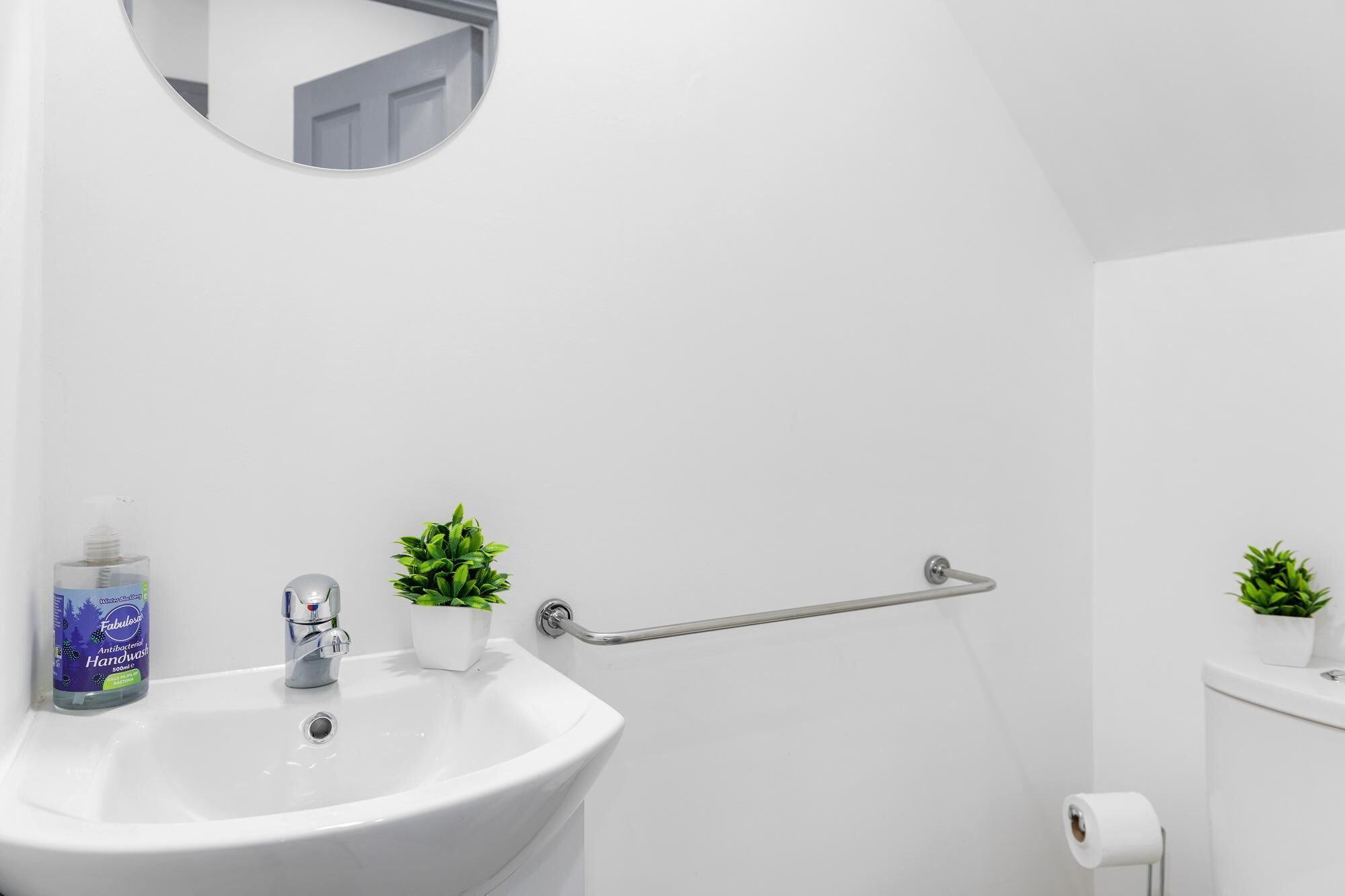 A bathroom with a white sink, a mirror, a hand sanitizer dispenser, and two potted plants.