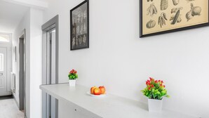 A modern hotel reception area with a white counter, framed botanical illustrations on the wall, and potted plants. - 3br-sleeps8-parking-wifi-closestation (Corby)