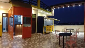 Una terraza en la azotea con un puesto de té, zona de estar y vistas de la ciudad de noche.