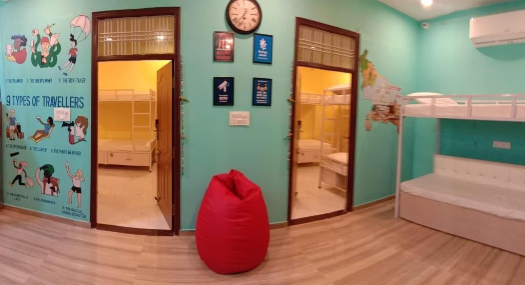 A room with bunk beds, a red bean bag chair, a wall clock, and a poster titled "9 Types of Travellers".