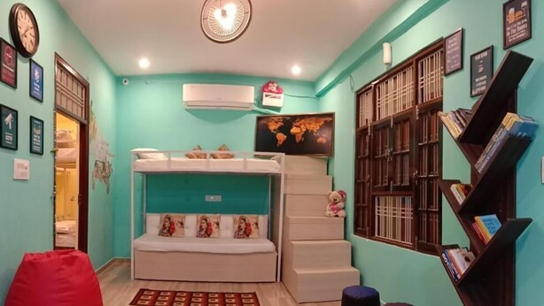 Una habitación con una cama individual superpuesta, una estantería y un sillón de cuero rojo.