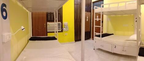 Una habitación con literas, una mesita de noche, una lámpara y un calentador de pared.