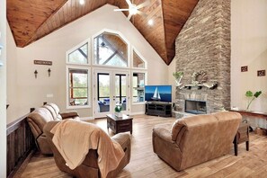 A spacious living room with a stone fireplace, leather sofas, and a large TV. - High Harbor Point on Quiet Cove (Seneca)