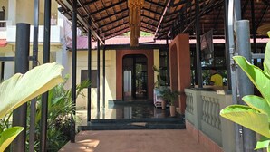 A covered walkway with a tiled floor, a central entrance, and a hanging light fixture. - Vinsons Cottages (Colva)
