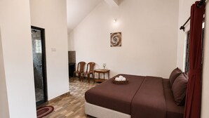 A bedroom with a bed, a small table with a vase, and a chair. - Vinsons Cottages (Colva)