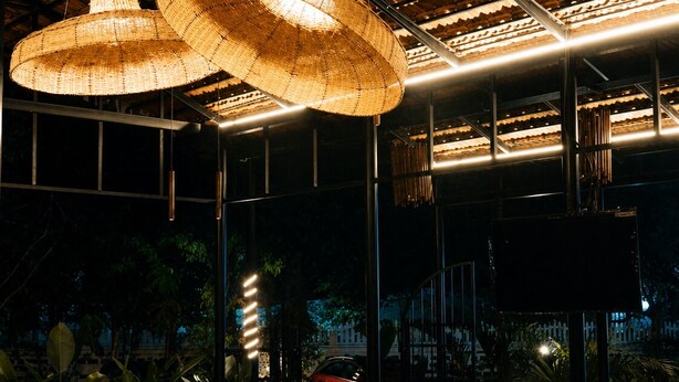 An indoor dining area with wicker ceiling lamps, a wooden dining table, and a bench seating area. - Vinsons Cottages (Colva)