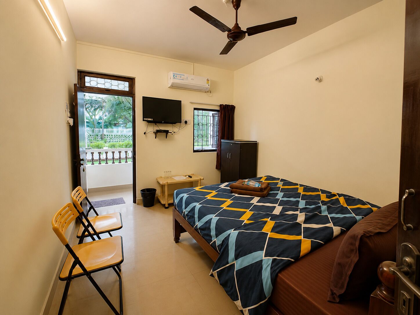 A bedroom with a bed, a desk, a chair, a television, and a ceiling fan.