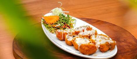 A wooden table with a white plate containing food and a small salad.